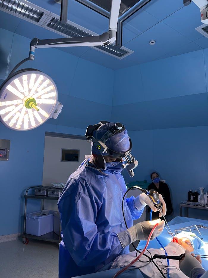 creative A surgeon in full gear conducts a procedure under bright lights in a blue-themed operating room.