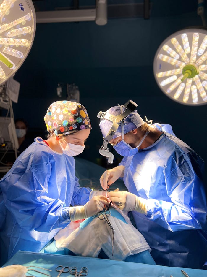 Services-02 Two surgeons focused on a procedure under bright surgical lights in a sterile operating room.